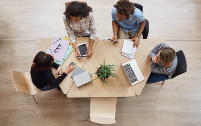 View from above of group young professional entrepreneurs sitting at table in coworking space, discussing profits of last team project, using laptop, digital tablet and smartphone